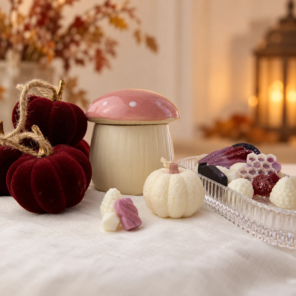 Quemador de cerámica con forma de seta, calabazas de terciopelo y wax melts de otoño sobre mantel de lino